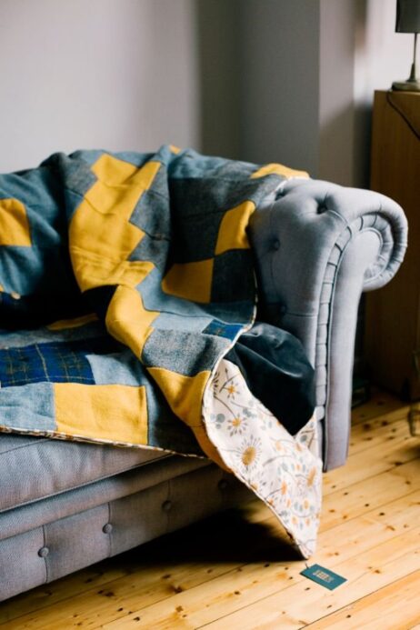 This quilt is stitched in a traditional strip design made from; sunshine yellow, grey and navy blue tartan Harris Tweed, trimmed with retro Hedgerow by renowned designer Angie Lewin and backed in a smoky grey velvet.